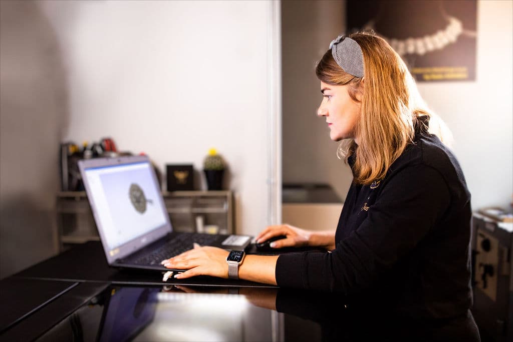 Jewelry designer working at a laptop displaying a jewelry model.
