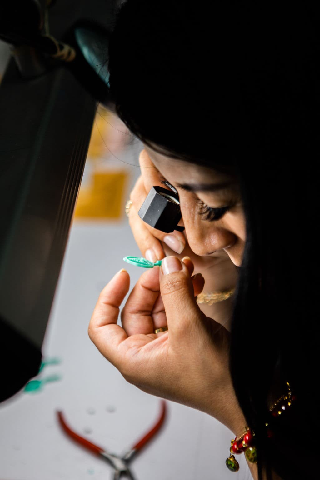 Jeweler closely examining a small green wax jewelry model through a loupe.